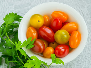 Mix of multicolored cherry tomatoes in a white porcelain bowl and parsley on a linen table napkin. Vegetables, vegetarian and healthy eating.