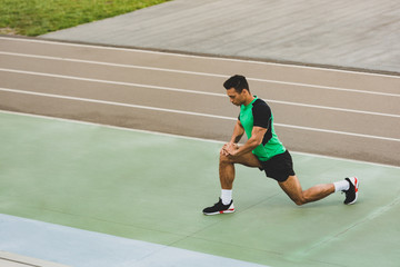 Obraz premium mixed race sportsman in sportswear stretching at stadium