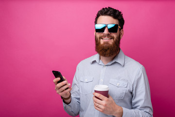 Portrait of happy man with beard in casual holding mobile phone and cup of coffee