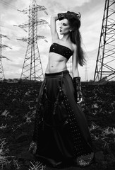 Informal fashion: lovely slim young gothic girl dressed in black leather skirt and gloves. Outdoor portrait in field near power line towers. Black and white