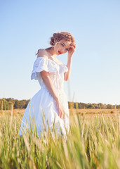 Portrait of pretty young sad woman wearing white dress in meadow