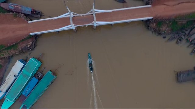 Aerial view of a motor boat passing under a bridge in Mekong river on the country side of Cambodia. A group of boats parked on the river.