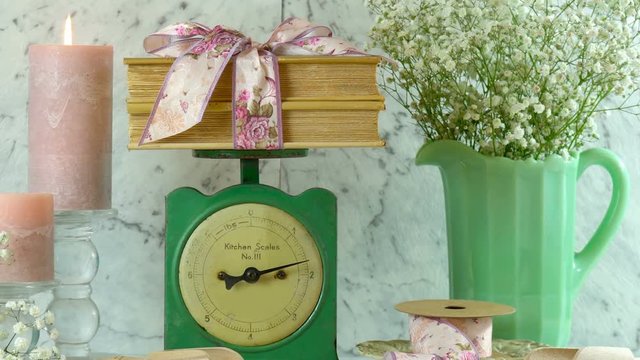 Vintage kitchen scale decor setting with porcelain jug of gypsophila flowers, candles, floral ribbons and old books.