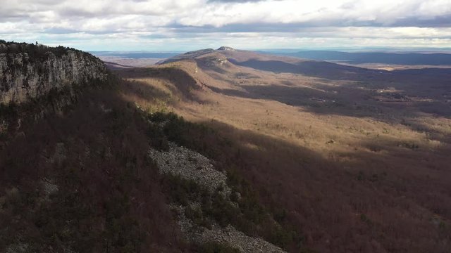 Drone flyover Catskill mountains with beautiful cloud shadows on a rocky cliff.  Bird of prey comes into frame towards the end. in $k.