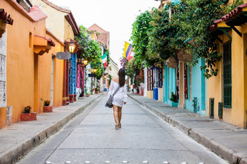 Fototapeta na wymiar Beautiful woman on white dress walking alone at the colorful streets of the colonial walled city of Cartagena de Indias