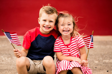 Cute siblings holding American flag while sitting on curb