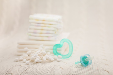 Close up baby hygiene items. stack of diapers, ear sticks, baby dummy and teether in selective focus