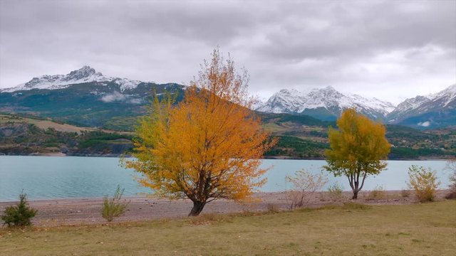 Autumn colors at a mountain lake, surrounded by snowy mountains. Location: French Alps. Filmed in 4K.