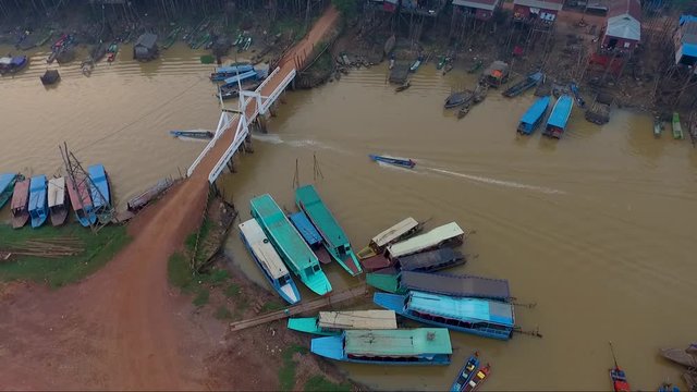 Aerial view of a motor boat passing under a bridge in Mekong river on the country side of Cambodia. A pile of boats parked on the river.