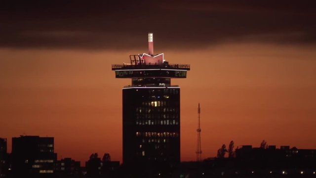 Slow pan up at sunset showing silhouette of A'DAM Toren (Adam Tower) in Amsterdam with plane flying in the background in the distance. Former shell tower in Saharan dust / sand red sky