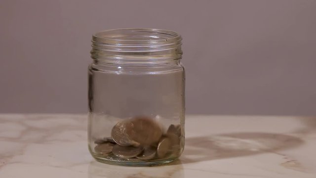 Continuous stream of coins dropping into a glass jar.