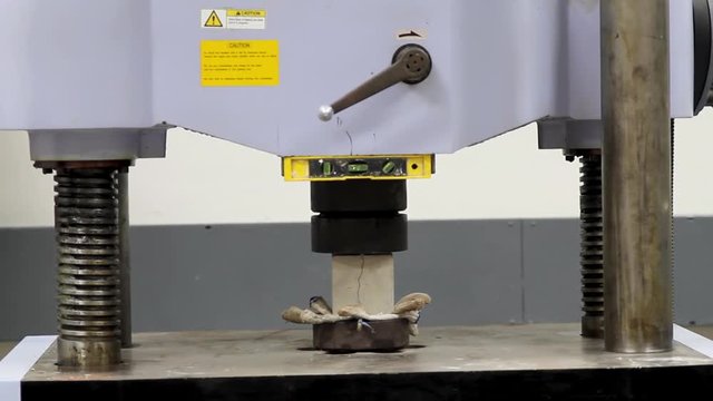 Concrete strength testing machine operating inside a laboratory.