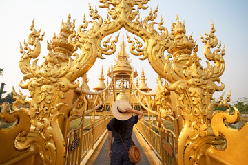 Hipster woman tourist is enjoy sightseeing travel inside golden norther gate inside War Rong Khun in Chiangrai, Thailand.