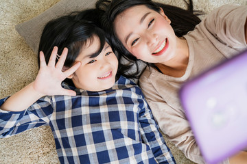 happy Asian Family mother  and daughter making a selfie photo while use  in living room home background.