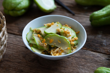 Fresh chayote fruits (Sechium edulis) stir fried with egg and garlic in bowl on wood background