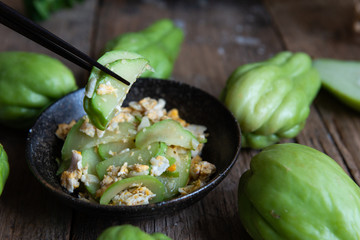 Fresh chayote fruits (Sechium edulis) stir fried with egg and garlic in bowl on wood background