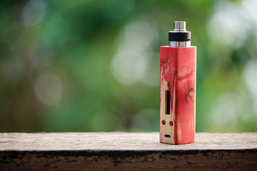 high end red natural stabilized wood box mods with rebuildable dripping atomizer on natural wood and green bokeh texture background, vaping device, selective focus