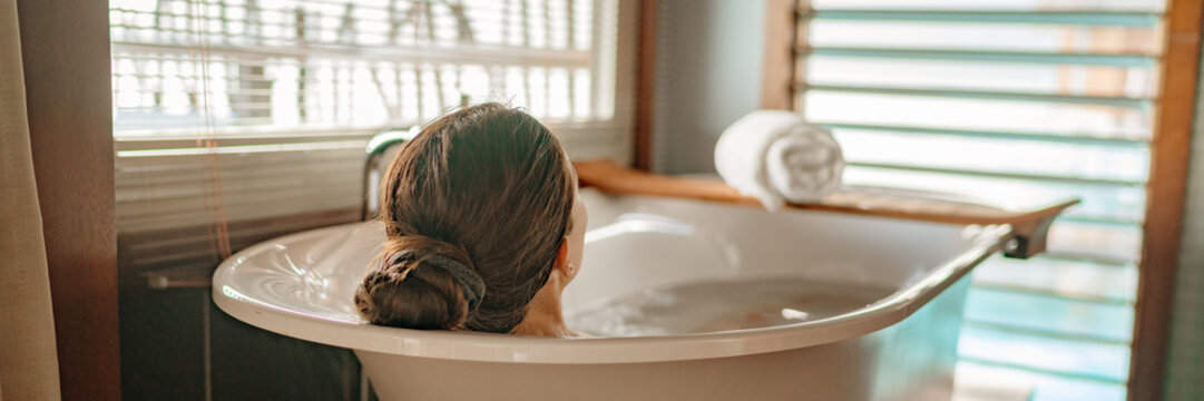 Luxury bath woman relaxing in hot bathtub in hotel resort suite room enjoying pampering spa moment lifestyle banner panorama.