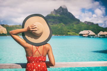 Beach vacation travel getaway summer holiday woman looking at view of Mt Otemanu on Bora Bora luxury hotel on romantic honeymoon. Tourist holding hat from behind enjoying Tahiti, French Polynesia. - obrazy, fototapety, plakaty