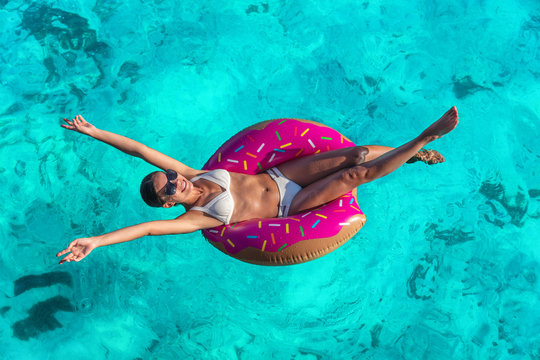 Summer vacation fun woman relaxing in donut swimming pool float with arms open in freedom and happiness enjoying tropical travel holidays in blue ocean background.