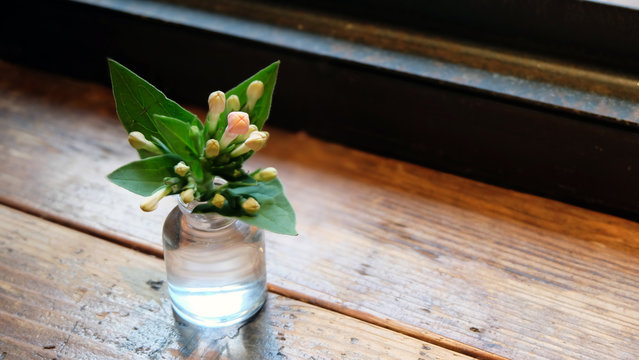 A small bouquet of flowers in a tiny jar on top of a wooden table.
