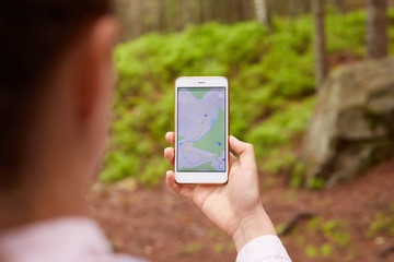 Woman standing in middle of nowhere, using navigation app on smartphone, following route with help of map, looking at device screen, using smartphone navigation while losing yourself in forest.