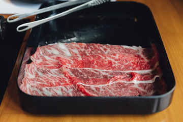 Premium Rare Slices Wagyu beef with high-marbled texture in black plate with tong for Sukiyaki and Shabu.