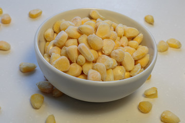 Bowl with frozen corn kernels on white background.