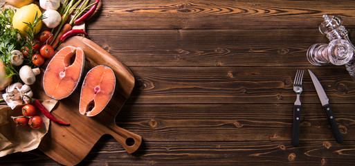 Fresh raw salmon fish steak with herbs and vegetables on wooden background