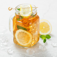 Iced tea with lemon slices and mint on light gray stone background.