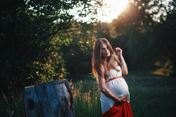 Young pregnant woman in the park outdoors. Calm pregnant woman in third trimester. Walking in...