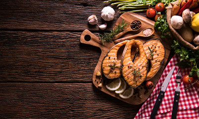 Grilled salmon fish with seasoning and various vegetables on cutting board on old wooden background