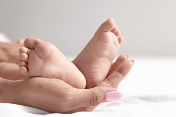 Mother holding her baby's feet on bed against light background, closeup. Space for text