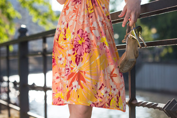 a young woman in a summer dress standing outside somewhere in the city near the river, holding...