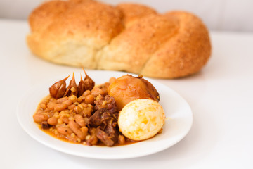 Challah Shabbat bread and hamin or cholent in hebrew - Sabbath traditional food on white table in the kitchen.