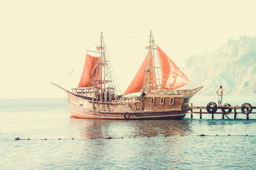 A ship with red sails at sea pier on the background of mountains