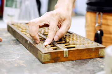 Closeup hand of person playing and demonstration used of ancient Chinese abacus on old black wooden table.