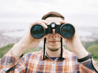 Traveler young man looking through binoculars outdoor, front view.