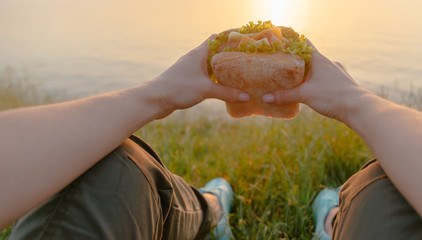 POV image of woman with burger on coastline.