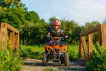 The little girl rides a quad bike. A mini quad bike is a cool girl in a helmet and protective clothing. Electric quad bike electric car for children popularizes green technology