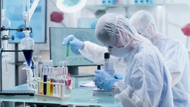 Two researchers in modern laboratory in coverall making some experiments. In the background - 3D brain simulation running on monitors