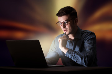 Young handsome businessman working late at night in the office with warm lights in the background