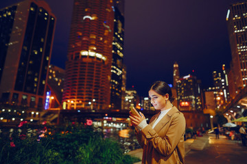 young brunette girl standing at night with phone by Chicago skyline