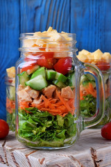 Layered salad with cheese, kale, carrot, chicken, cucumbers and cherry tomatoes in glass mason jars