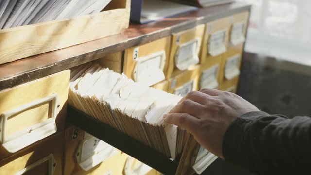 Man opens database drawer. Young librarian opens library card index. Archive, database, library concept.