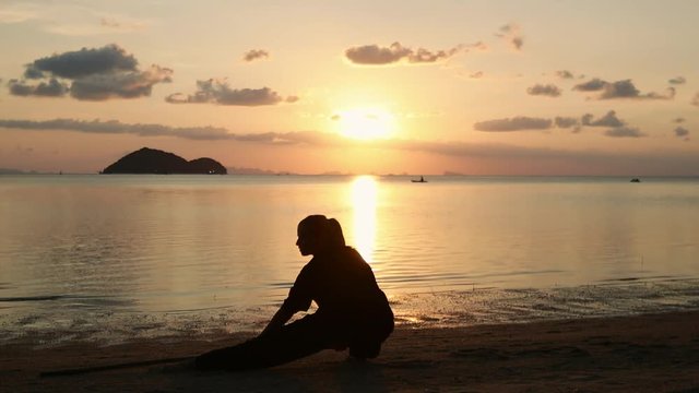 Silhouette of a young powerful woman on the beach doing a kung-fu exercises with a stick on the background of the sea.