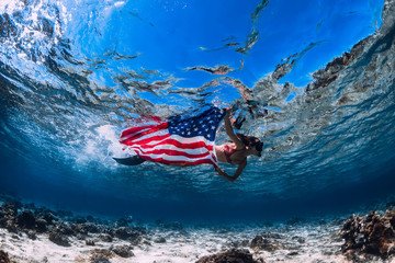 Beautiful girl freediver swim over sandy sea bottom with United States flag. Independence day.