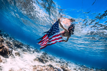 Beautiful girl freediver swim over sandy sea bottom with United States flag. Independence day.