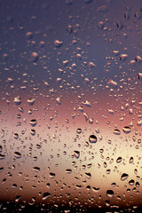 Macro photo of raindrops on glass against a blurred sunset blue violet pink orange red black...
