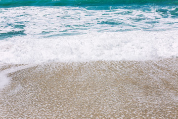 Turquoise sea wave with foam on the sandy beach. Close-up, background. Space for text.